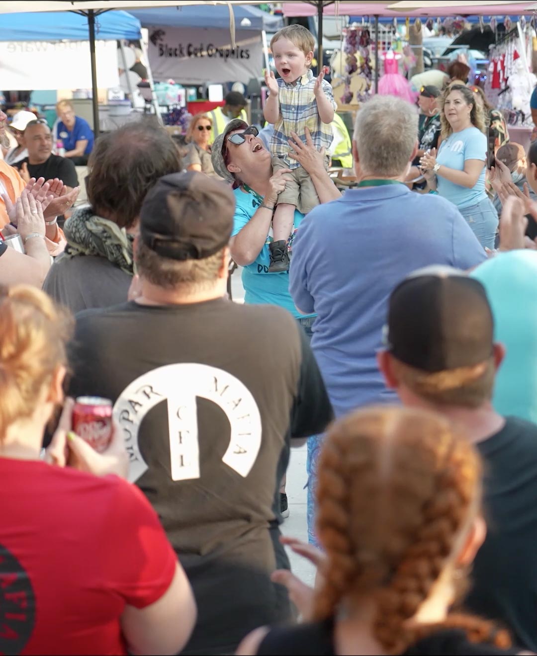 Crowd cheers with a young boy on his mother’s shoulders at the Mopar Mafia Car and Truck Show for the Autism Society of Greater Orlando.