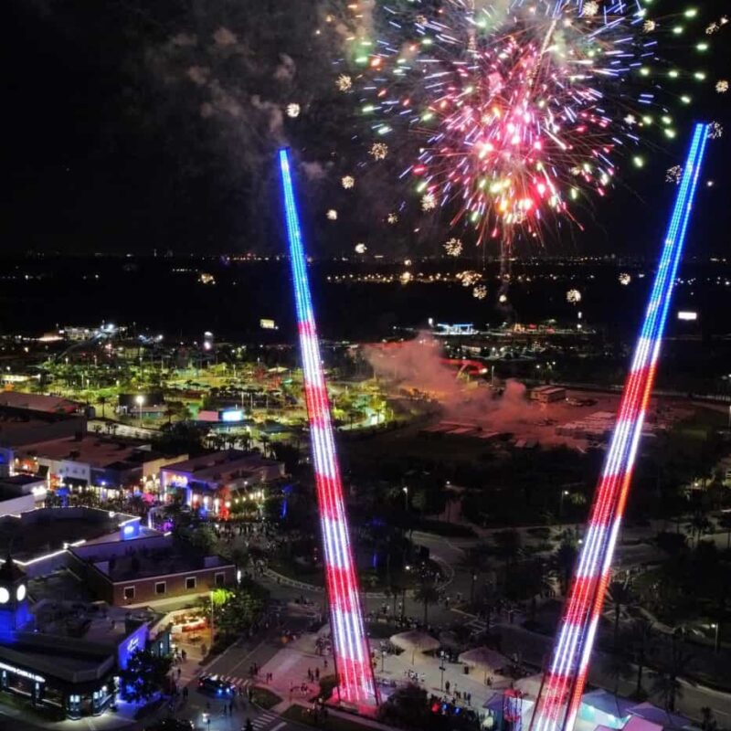 Sunset Walk Slingshot ride lit up at night with stars and stripes under 4th of July fireworks