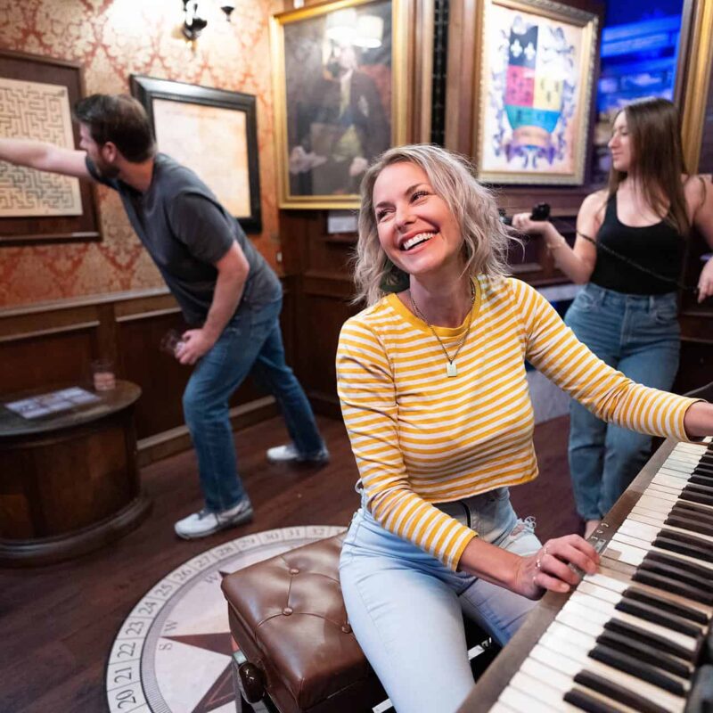 Group solving puzzles involving a piano and framed maze in an Escapology escape room