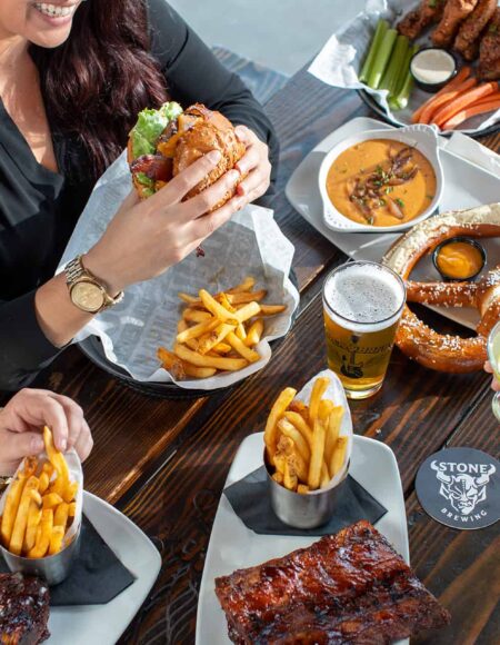 People dining at Rock & Brews at a table with ribs, fries, wings, and a giant pretzel