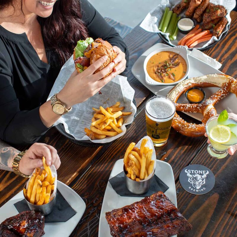 People dining at Rock & Brews at a table with ribs, fries, wings, and a giant pretzel