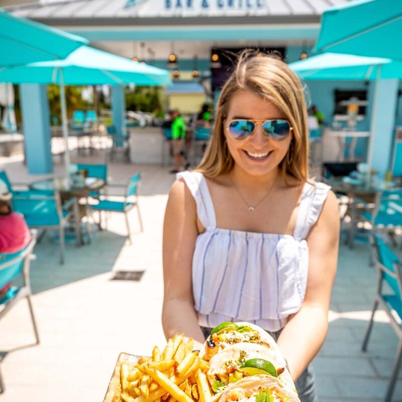 Woman holding a plate of fish tacos and fries at Salty Rim Bar and Grill