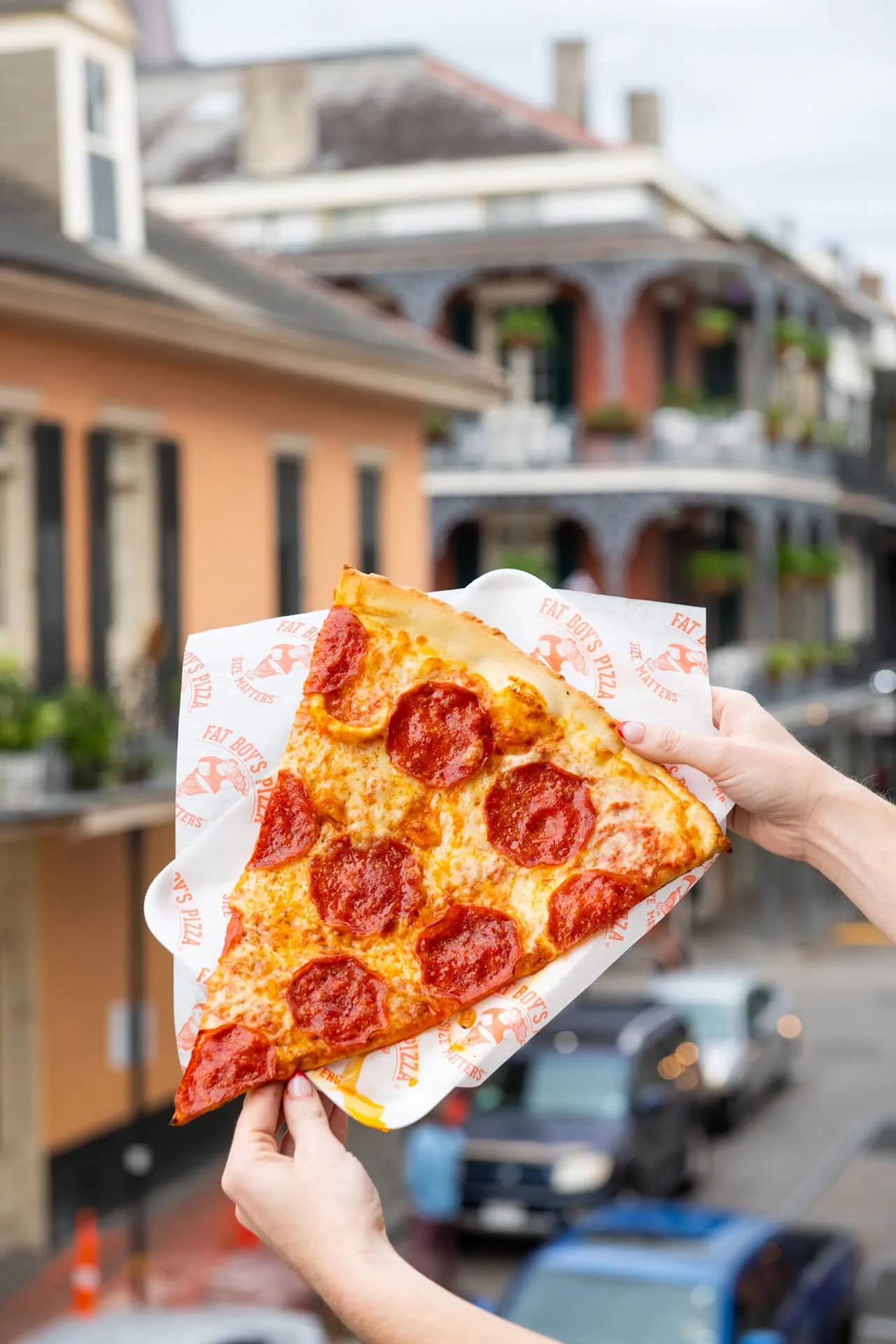 Hands holding a large slice of Fat Boy’s Pizza