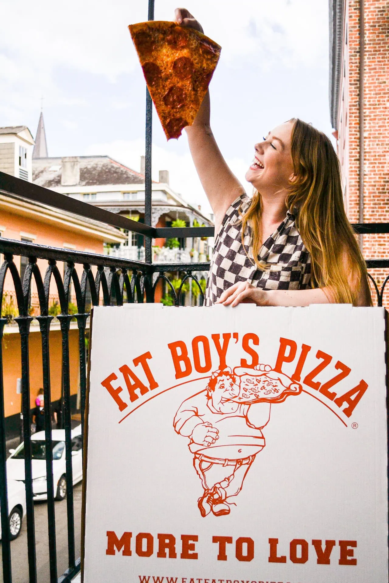Smiling woman holding a large slice of Fat Boy’s Pizza