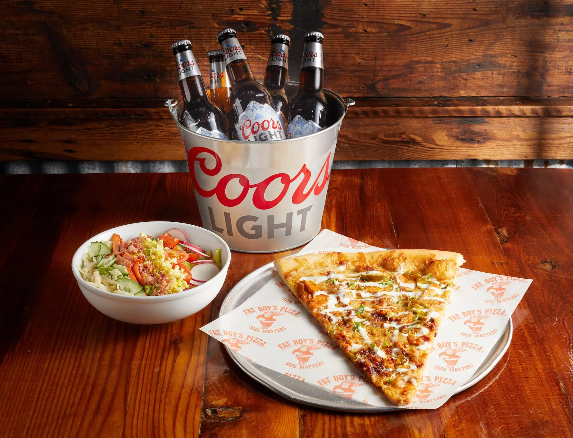 Slice of Fat Boy’s Pizza with a side salad and a bucket of bottled Coors Light beer